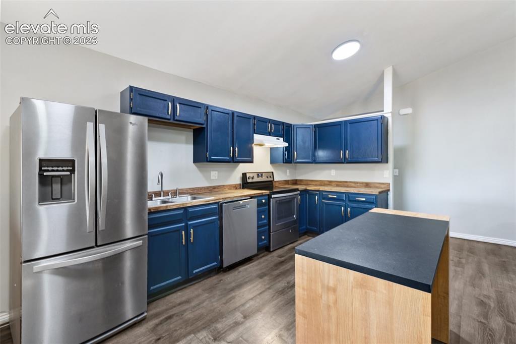 Image 24 of 27: Kitchen with blue cabinetry, stainless steel appliances, wood-finish floori