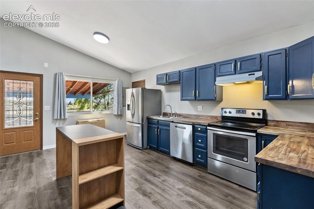 Image 7 of 27: Vaulted ceilings, wood-finish flooring, blue cabinetry, stainless steel app