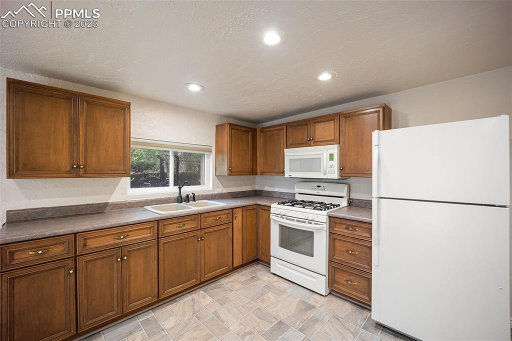 Image 11 of 31: Kitchen with white appliances, brown cabinets, stone finish flooring, a tex
