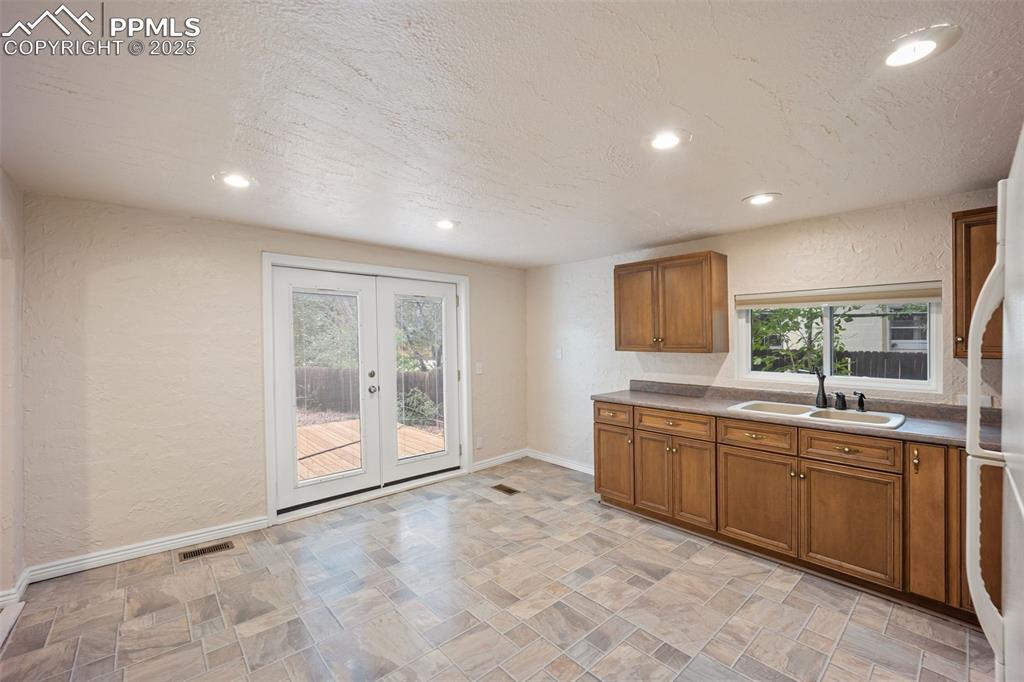 Image 13 of 31: Kitchen with a textured wall, brown cabinetry, french doors, recessed light