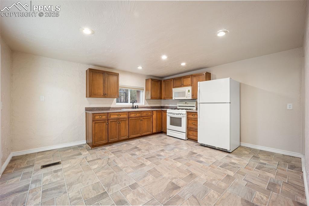 Image 14 of 31: Kitchen featuring white appliances, brown cabinets, recessed lighting, ston