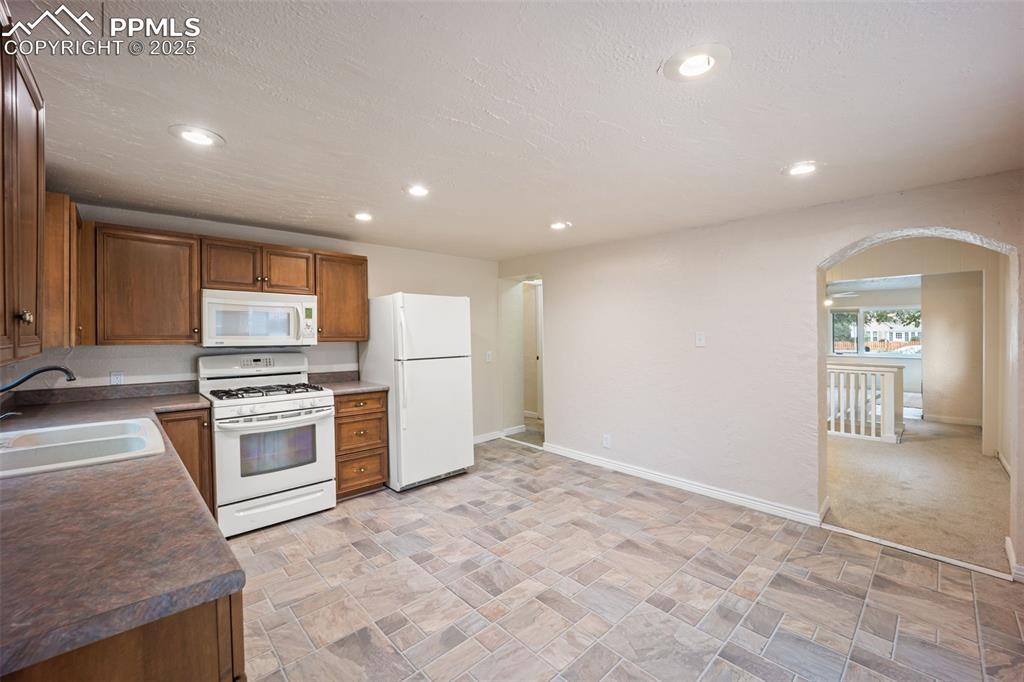 Image 15 of 31: Kitchen with white appliances, arched walkways, recessed lighting, dark cou