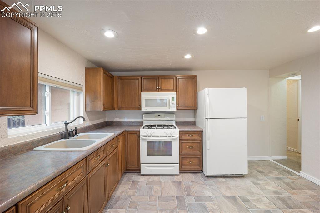Image 16 of 31: Kitchen with white appliances, brown cabinets, recessed lighting, stone fin
