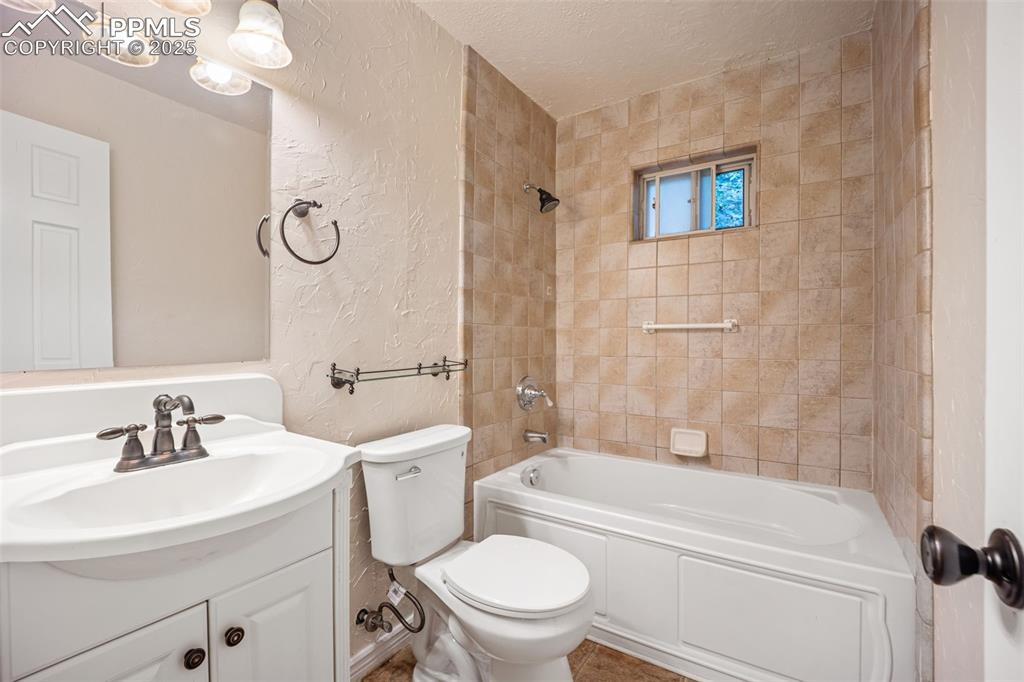 Image 19 of 31: Full bath with a textured wall, vanity, shower / bath combination, and a te