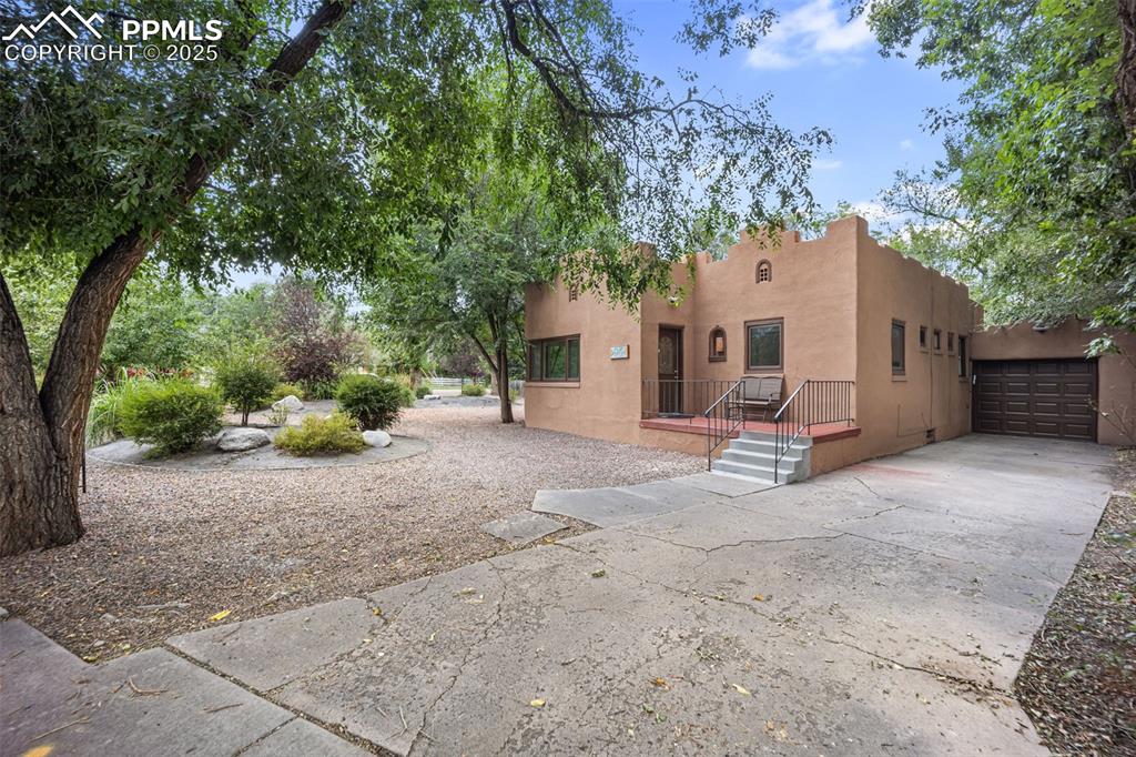 Image 4 of 31: Rear view of property with stucco siding, a garage, and concrete driveway
