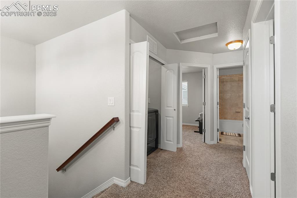 Image 10 of 22: Hall with an upstairs landing, carpet flooring, attic access, and washer /