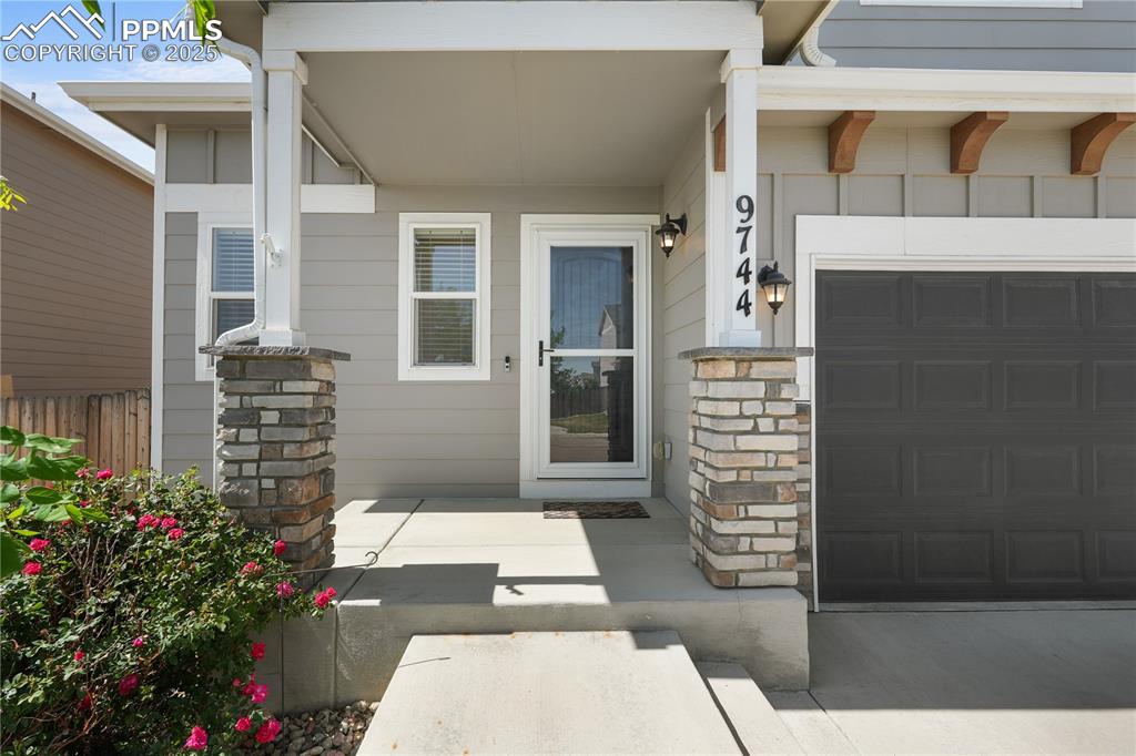 Image 4 of 22: Entrance to property with stone siding, a garage, and concrete driveway