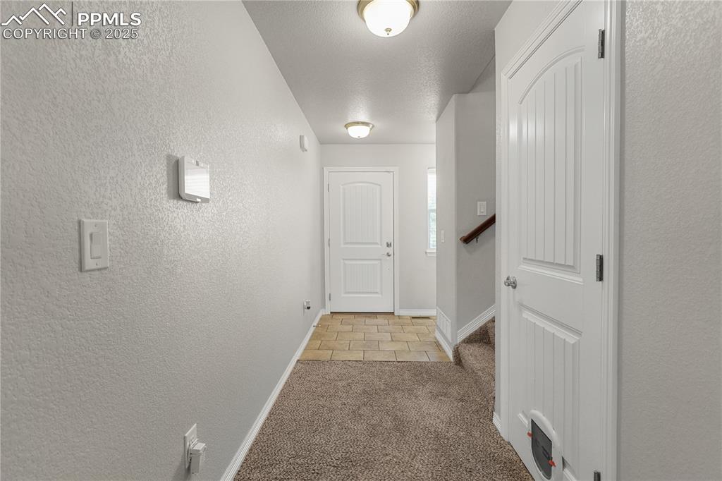 Image 5 of 22: Hall with light colored carpet, a textured wall, and light tile patterned f