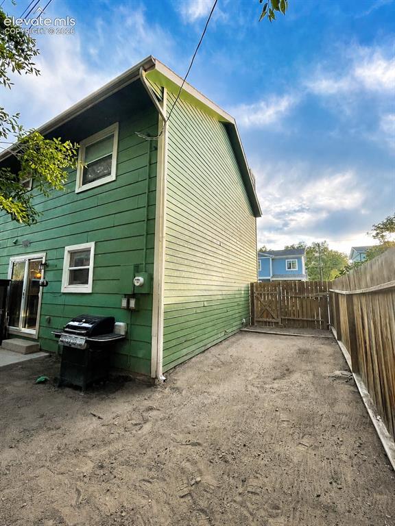 Image 24 of 27: Rear exterior featuring green horizontal siding, white trim, and a fenced y