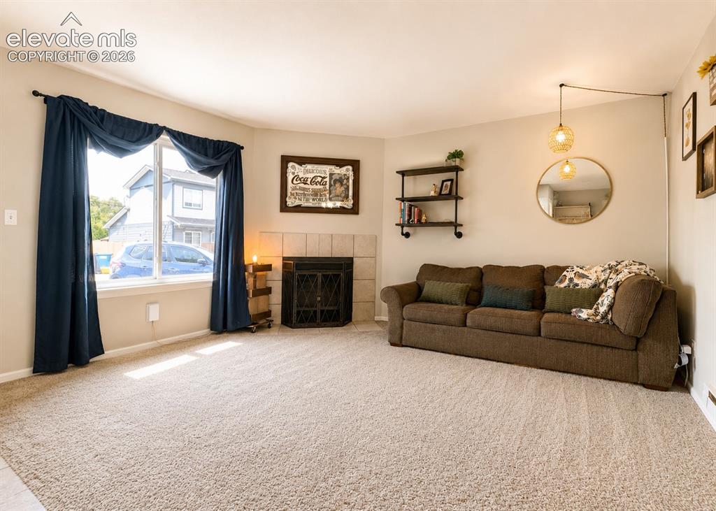 Image 3 of 27: Carpeted living area featuring a corner window, a fireplace with a tiled su