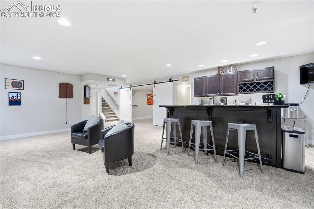 Image 33 of 50: Living area featuring a barn door, bar, light carpet, and recessed lighting