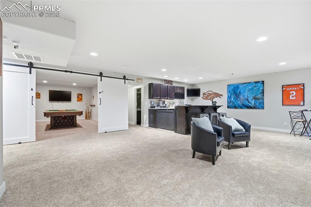 Image 34 of 50: Living area with a barn door, bar with sink, light carpet, recessed lightin