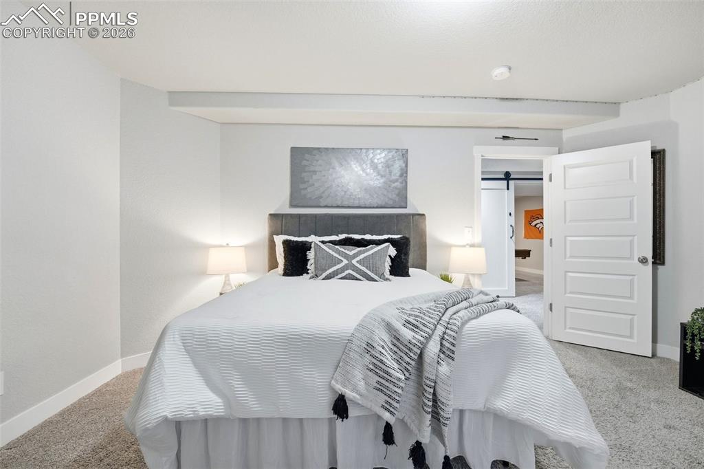Image 36 of 50: Bedroom with light colored carpet and a barn door