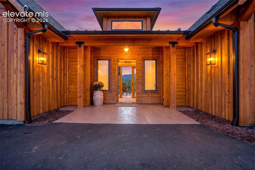 Image 2 of 50: Wood-clad exterior with a covered entry, multiple exterior wall sconces, an