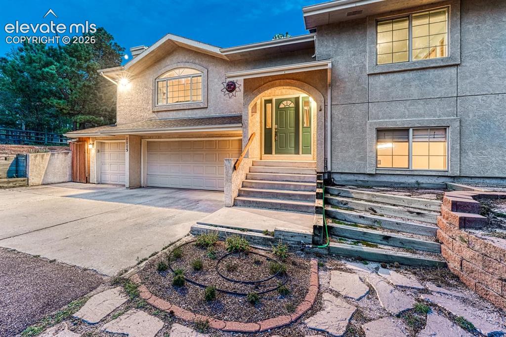 Image 2 of 46: Stucco home with concrete and paved driveway and thoughtfully landscaped.