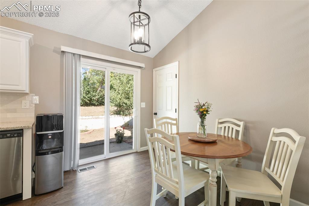 Image 15 of 28: Dining room featuring dark wood-type flooring, lofted ceiling, and a chande