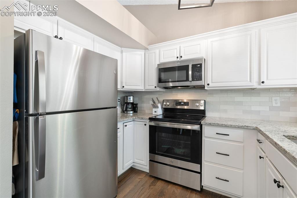 Image 20 of 28: Kitchen with stainless steel appliances, white cabinets, light stone counte