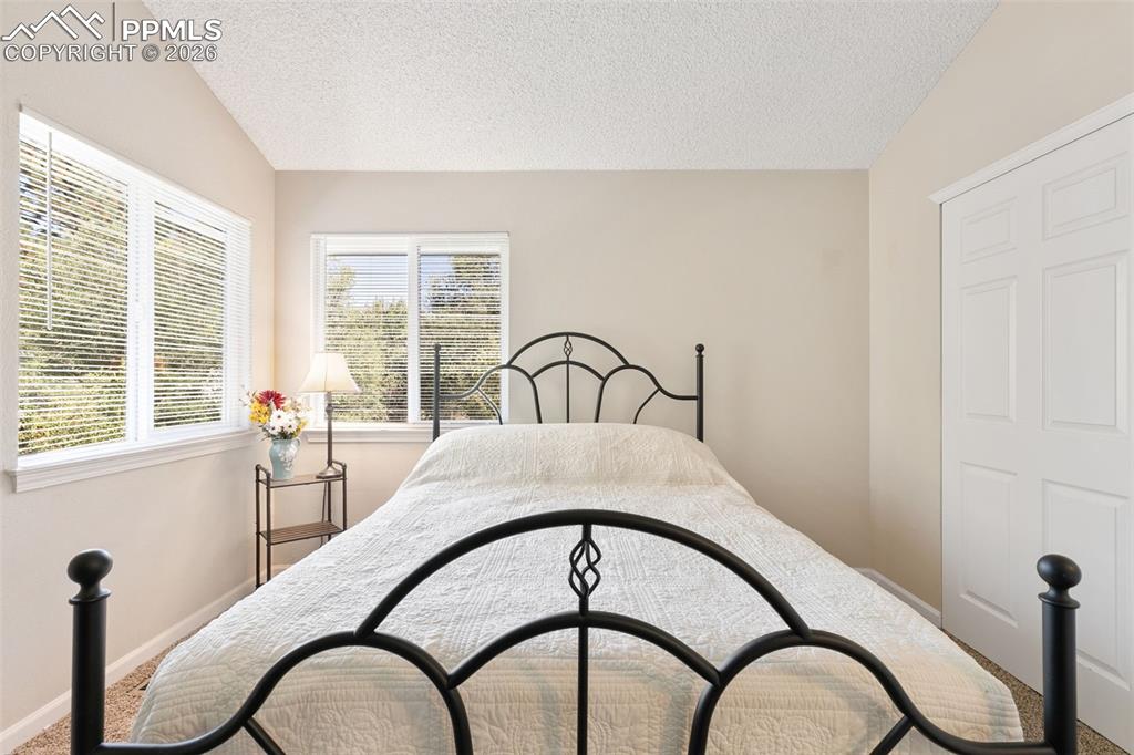Image 24 of 28: Carpeted bedroom with lofted ceiling and a textured ceiling
