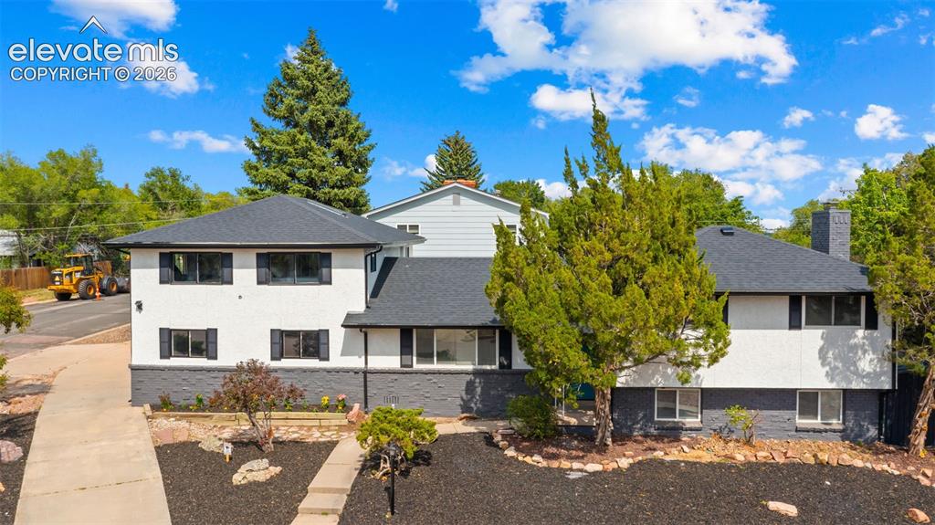Caption: Split-level residence featuring a white stucco exterior with a dark gray lower level, contrasting bl