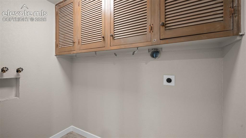 Image 26 of 45: Laundry area featuring louvered wood-finish cabinetry, neutral wall tones,