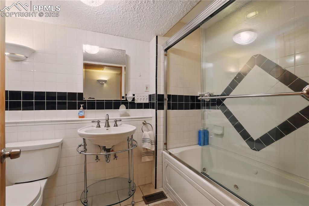 Image 34 of 50: Hall bath with a jetted tub and glass shower doors