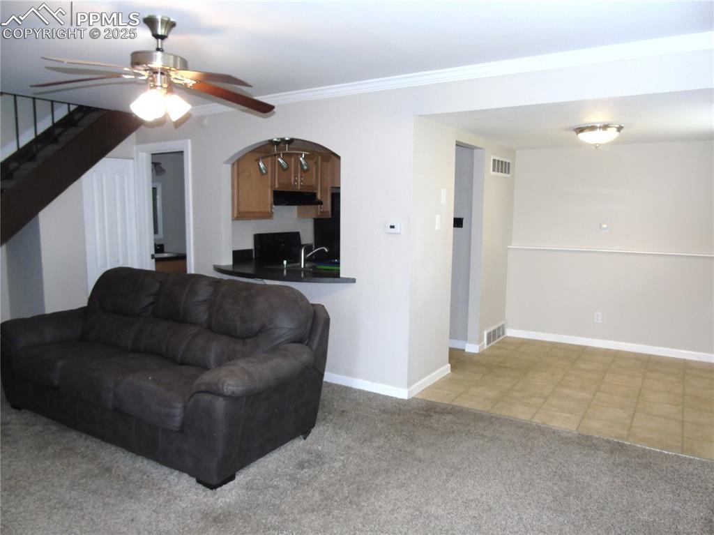 Image 2 of 29: Living area with light carpet, ceiling fan, stairway, ornamental molding, a
