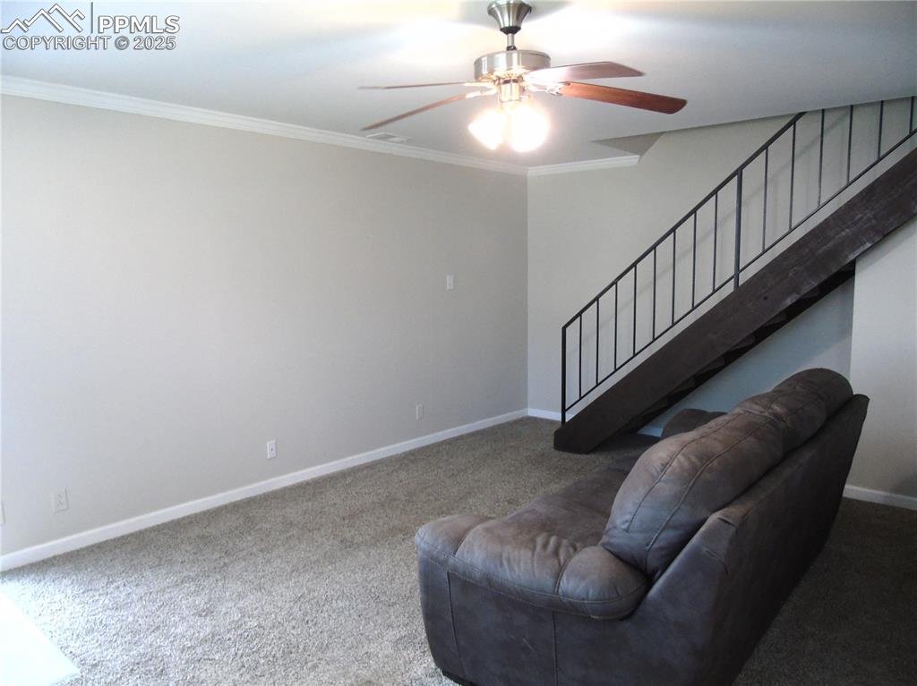 Image 5 of 29: Carpeted living area with crown molding, a ceiling fan, and stairway
