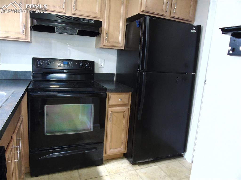 Image 9 of 29: Kitchen with black appliances, dark countertops, under cabinet range hood,