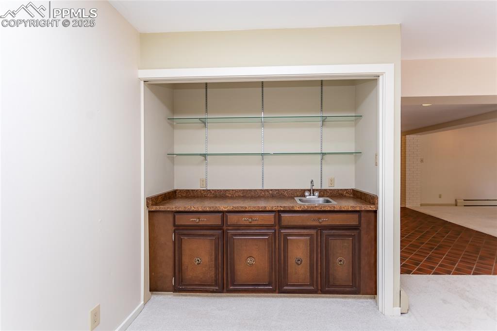 Image 6 of 35: Indoor wet bar featuring light carpet, open shelves, dark countertops, and 