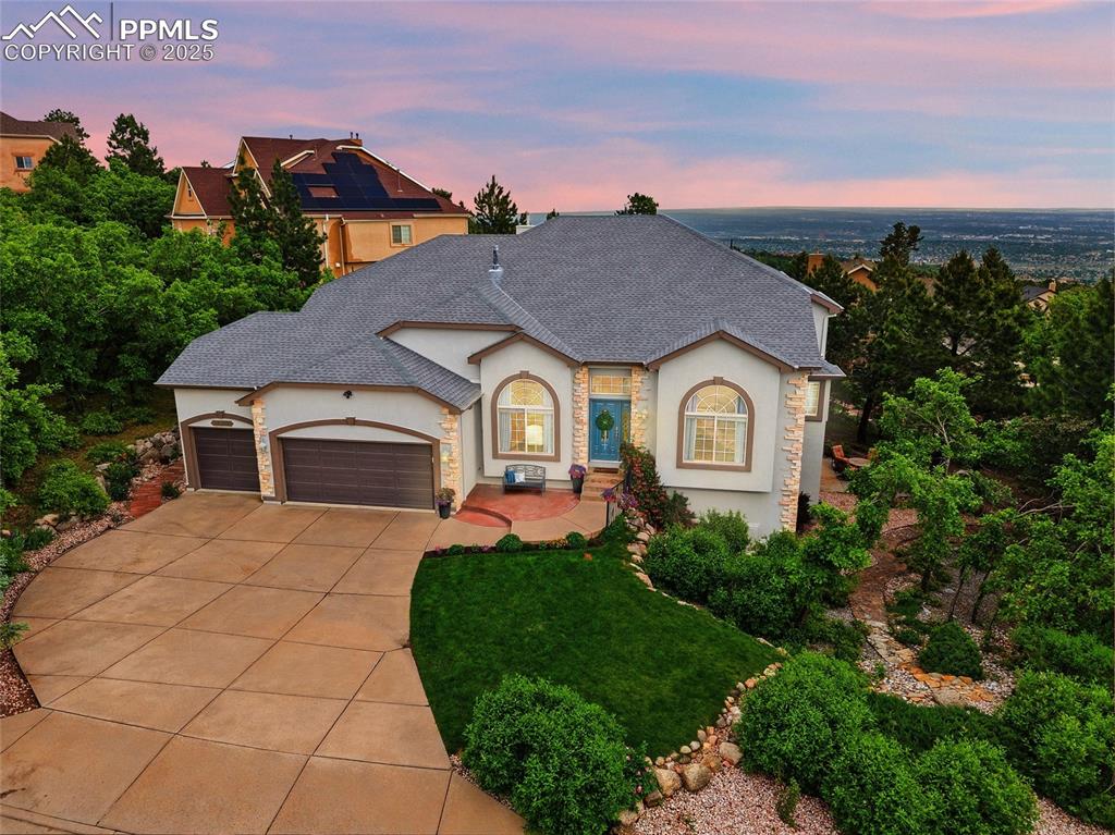 Caption: Twilight photo of front of home with stucco siding, a 3 car garage, gorgeous landscaping, and view o