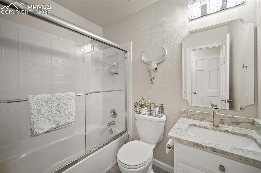 Image 30 of 50: Full bathroom with vanity, enclosed tub / shower combo, toilet, and a textu