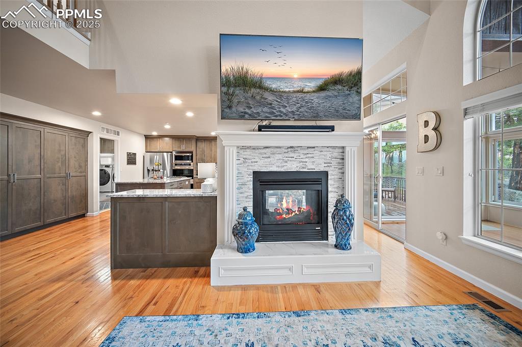 Image 9 of 50: Living room with wood floors, vaulted ceilings, gorgeous windows, and a gas