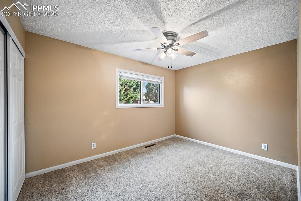 Image 19 of 38: Bedroom 1 with ceiling fan, large window and closet.