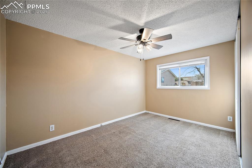 Image 21 of 38: Bedroom 2 large window, carpet and ceiling fan.