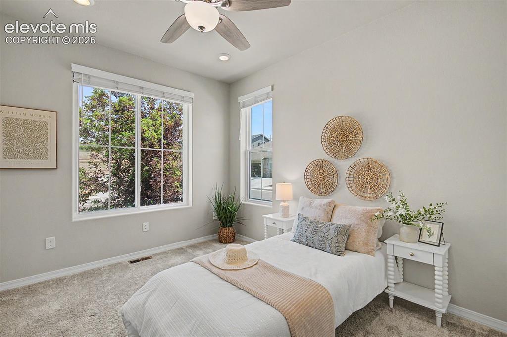 Image 28 of 45: Bright bedroom featuring two windows, light gray walls, and plush carpet fl