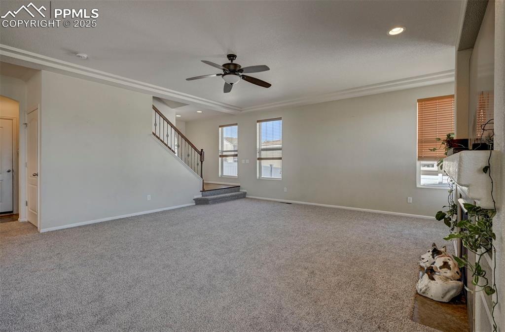 Image 21 of 50: Unfurnished living room with a ceiling fan, carpet floors, stairs, and rece