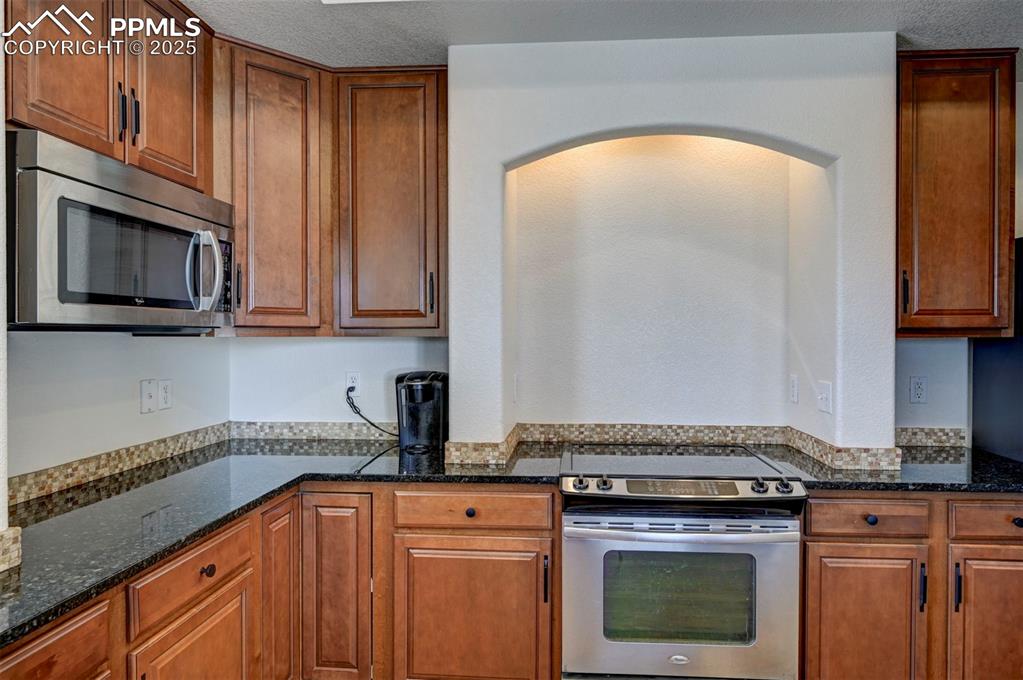 Image 30 of 50: Kitchen with appliances with stainless steel finishes, arched walkways, dar