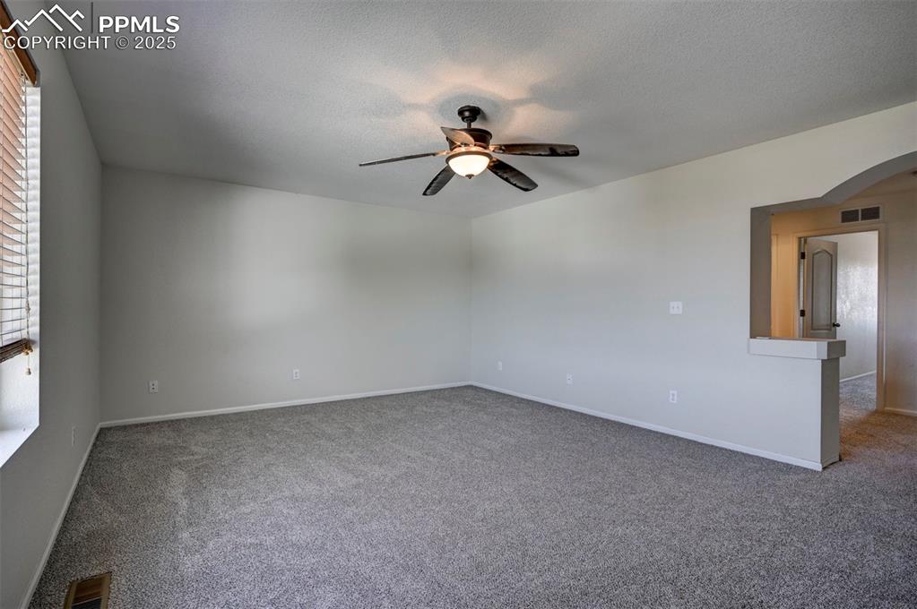 Image 35 of 50: Carpeted empty room featuring a ceiling fan, arched walkways, and a texture