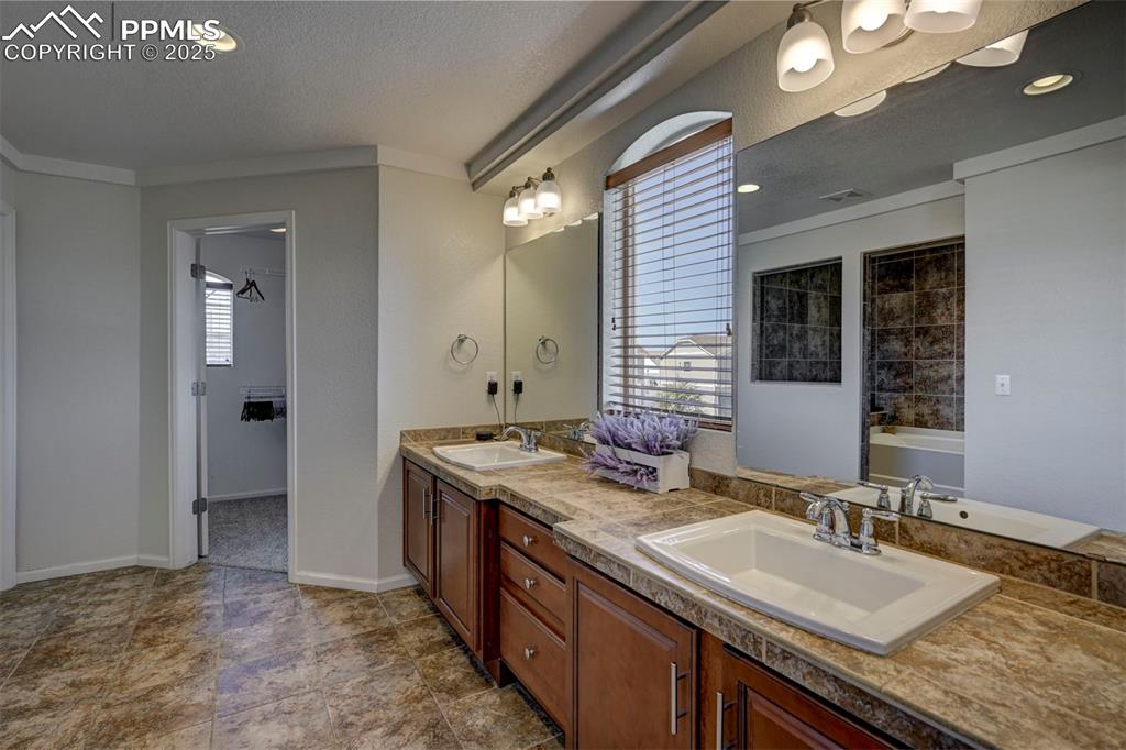 Image 44 of 50: Bathroom featuring double vanity, a bathtub, ornamental molding, a textured