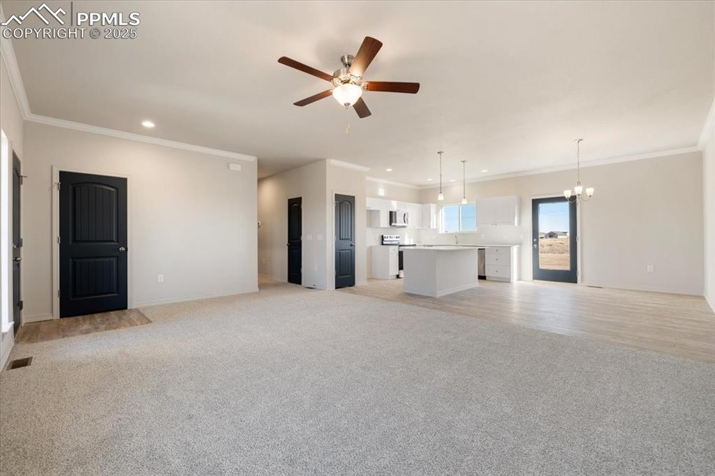 Image 4 of 22: Unfurnished living room featuring light carpet, crown molding, a chandelier