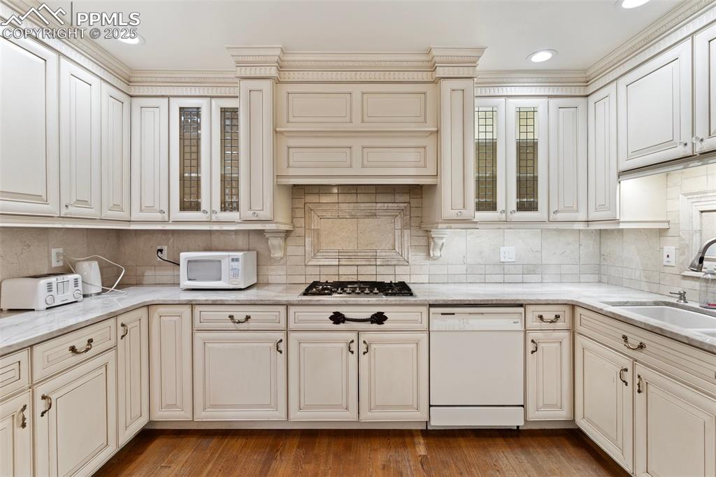Image 18 of 50: Kitchen with white appliances, cream cabinets, backsplash, crown molding, a