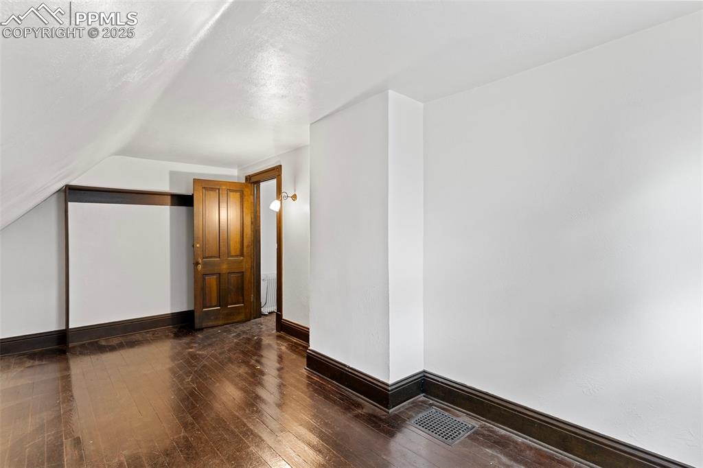 Image 39 of 50: Unfurnished room with dark wood-type flooring and lofted ceiling