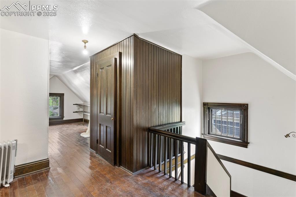 Image 42 of 50: Hall featuring an upstairs landing, vaulted ceiling, radiator, and hardwood