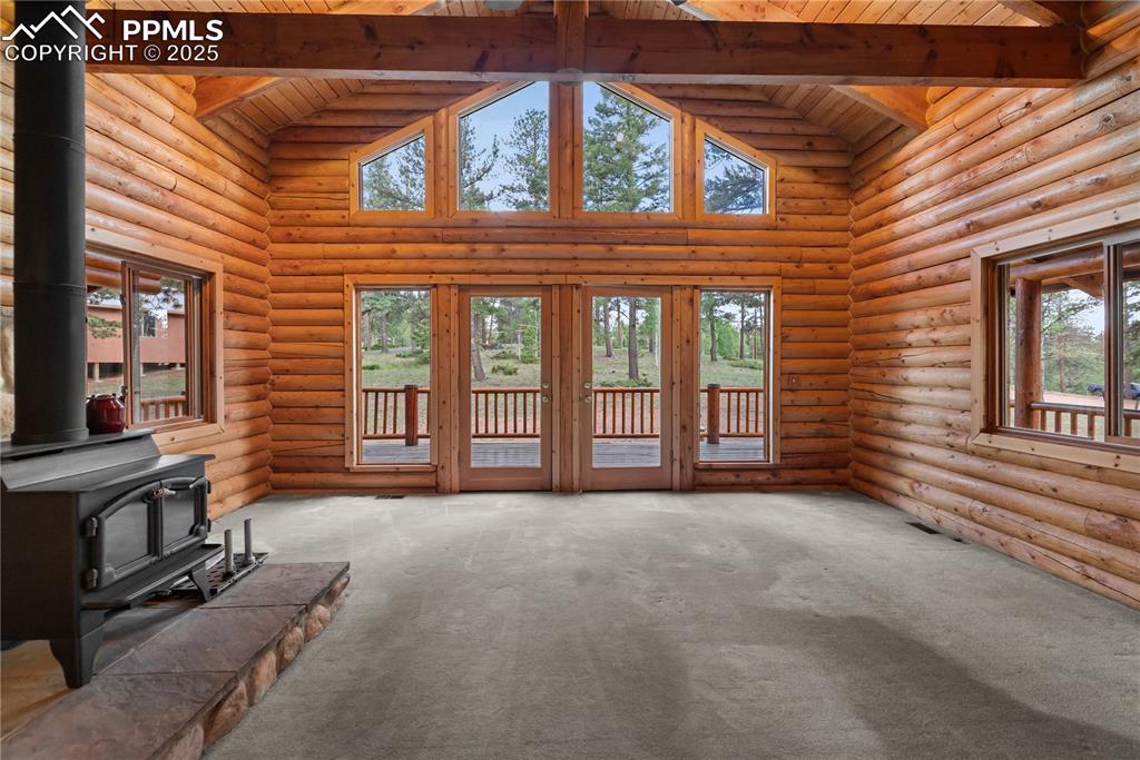 Image 15 of 45: Unfurnished living room with a wood stove, a wooden ceiling with exposed be