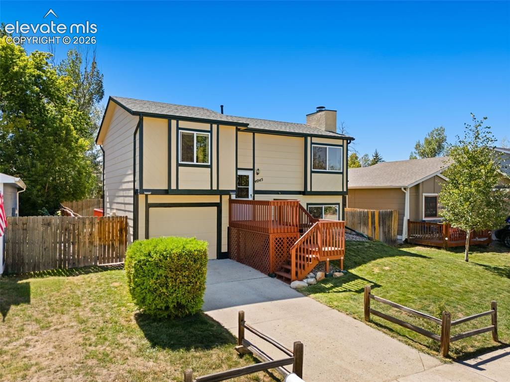Caption: Split-level exterior with a two-car garage, front-facing deck, and mature landscaping