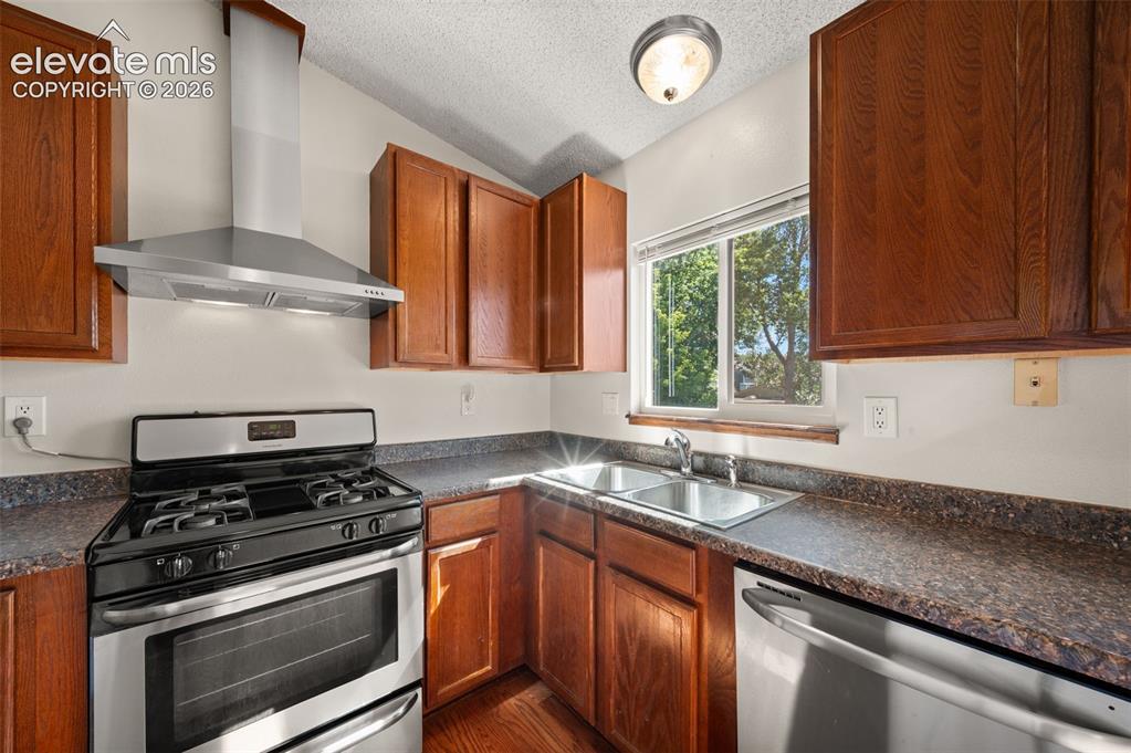 Image 14 of 40: Galley kitchen featuring wood cabinetry, stainless steel appliances, dual b