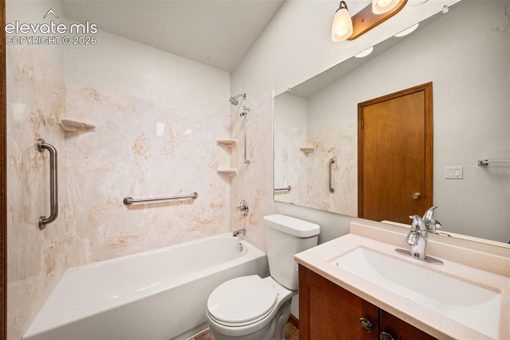 Image 17 of 40: Built-in tub with textured wall surround, integrated shelves, and grab bars