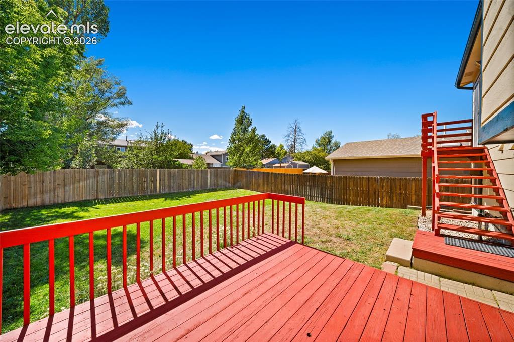 Image 31 of 40: Expansive backyard featuring a stained wood deck, red painted railings, and