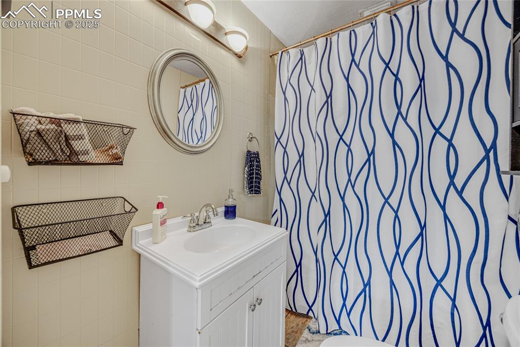 Image 18 of 31: Bathroom featuring tile walls, vanity, and a shower with curtain
