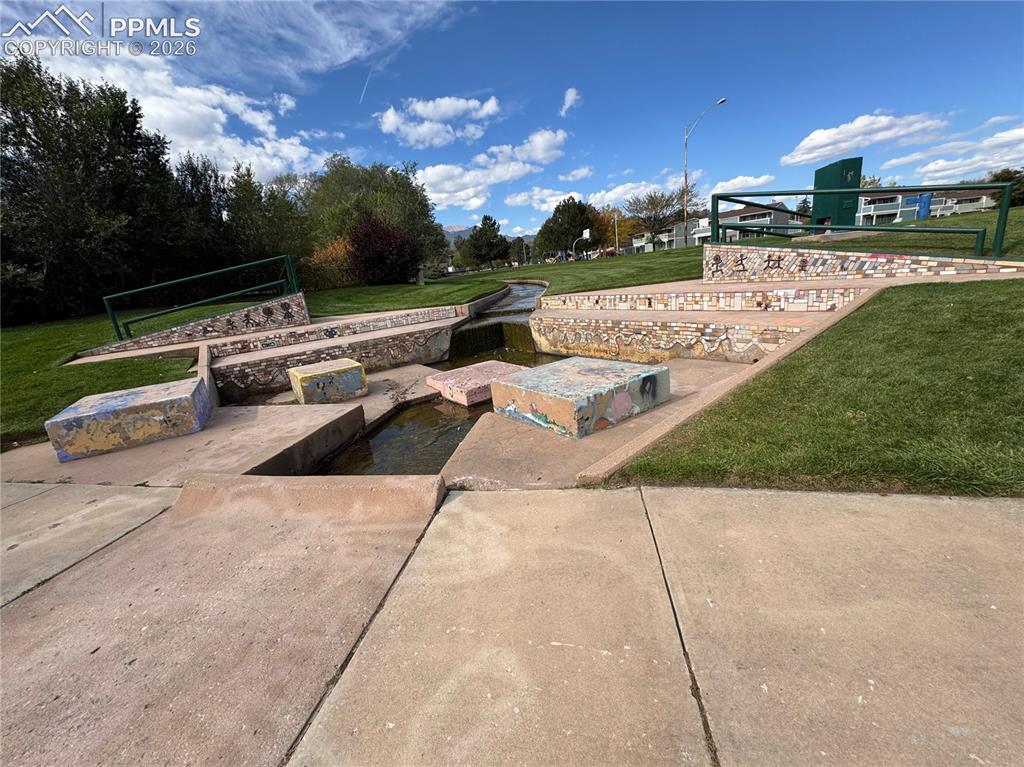 Image 23 of 27: Concrete pathway bordering a tiered water feature with mosaic tile accents 
